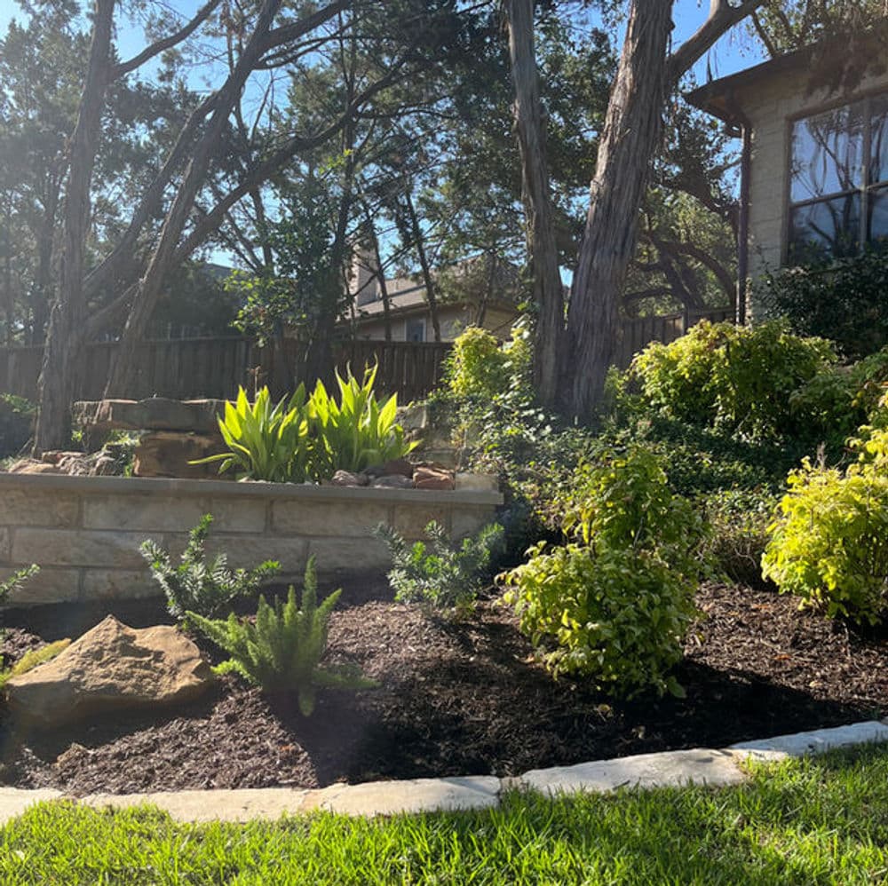 Lush garden with stone planters, greenery, and sunlight filtering through trees.