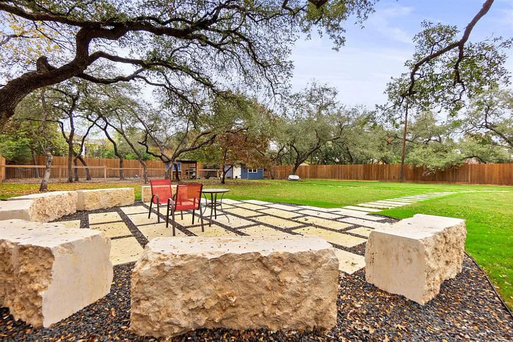 Outdoor seating area with stone fire pit and cozy chairs surrounded by lush greenery.