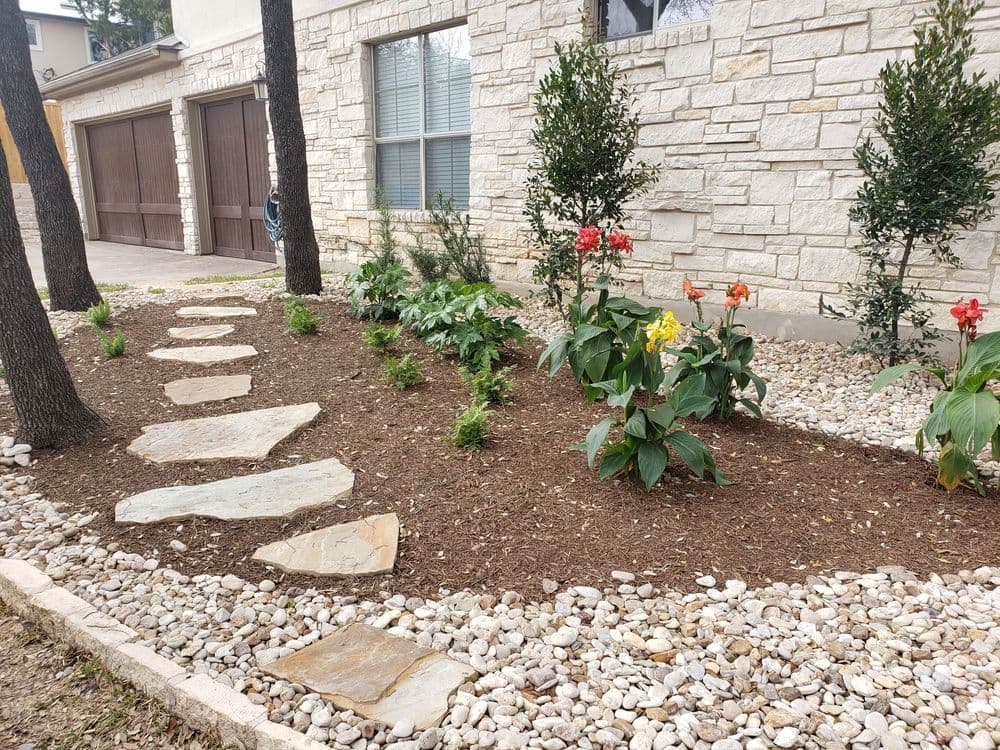 Landscaped garden with flower beds, stone path, and decorative rocks by a modern home.