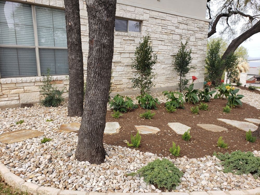 Landscaped garden with stone path, shrubs, and colorful flowers near a stone building.
