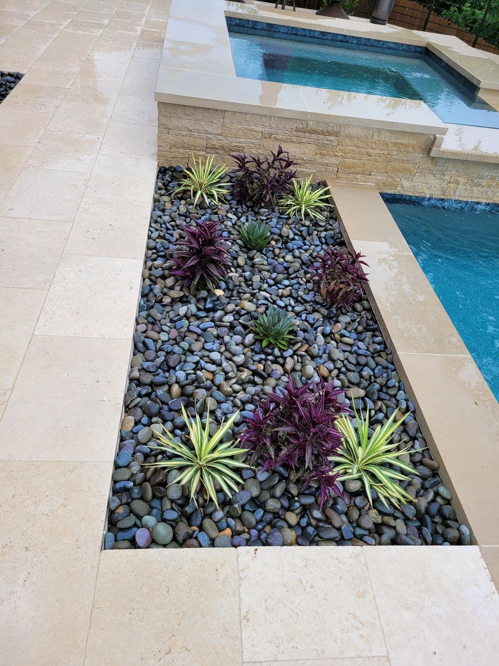 Modern backyard landscaping with colorful plants and smooth stones near a pool.
