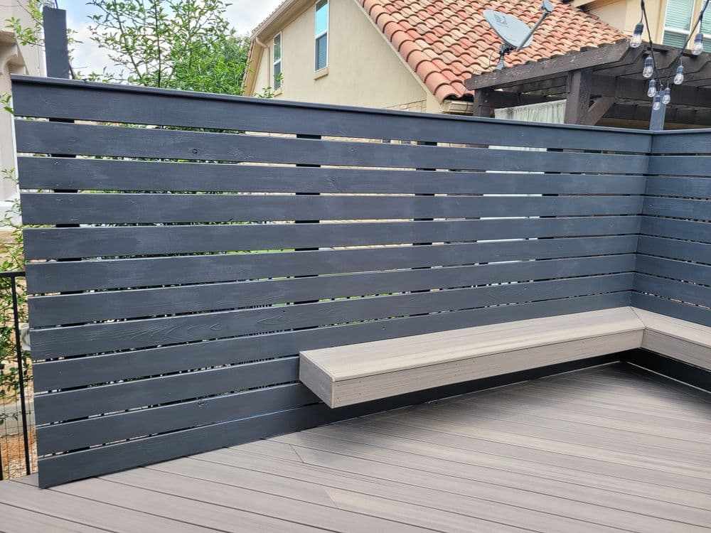 Modern wooden fence panels with a bench and composite decking in a backyard setting.
