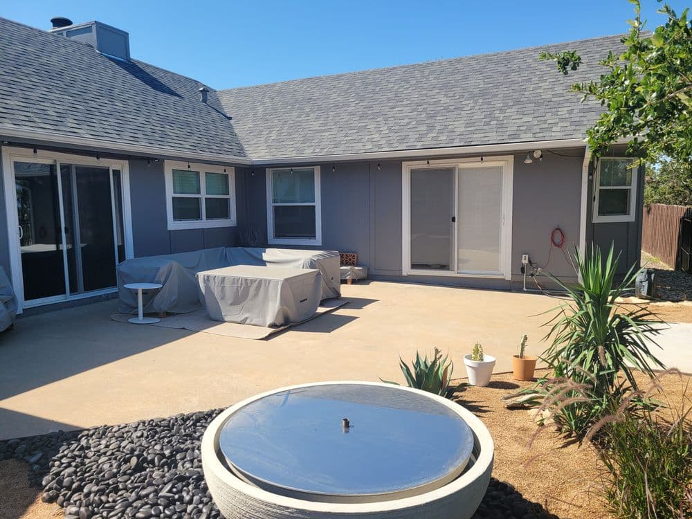Modern backyard patio with covered seating, decorative plants, and a stone water feature.